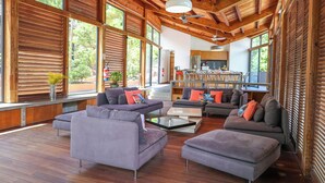 A spacious living area with a wooden ceiling and large windows, a kitchen in the background, and a modern seating arrangement. - Villa Nou Cinq, jungle view, swimming pool and beach 5 min away (Le Gosier)