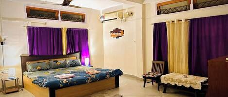 A bedroom with a bed, a desk, a chair, a ceiling fan, and a window with purple curtains.
