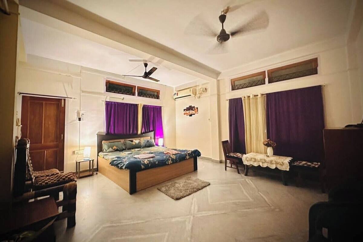 Ein Schlafzimmer mit Bett, Deckenventilator, Schreibtisch mit Stuhl und Fenster mit Vorhängen.