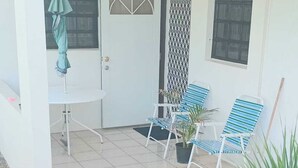 Una veranda coperta con due sedie a righe blu, un tavolino e un ombrello verde.