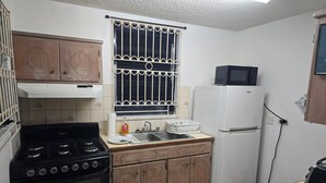 Una cucina compatta con piano cottura a gas, frigorifero bianco e forno a microonde.
