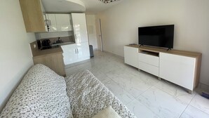 Ein modernes Wohnzimmer mit einer Couch, einem Flachbildfernseher und einer Küchenzeile mit Schränken und einer Kaffeemaschine.
