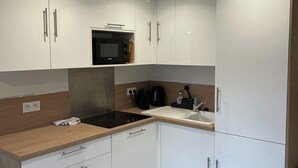 Eine kleine Küche mit weißen Schränken, einer schwarzen Mikrowelle, einer Holz Arbeitsplatte und einem Spülbecken.