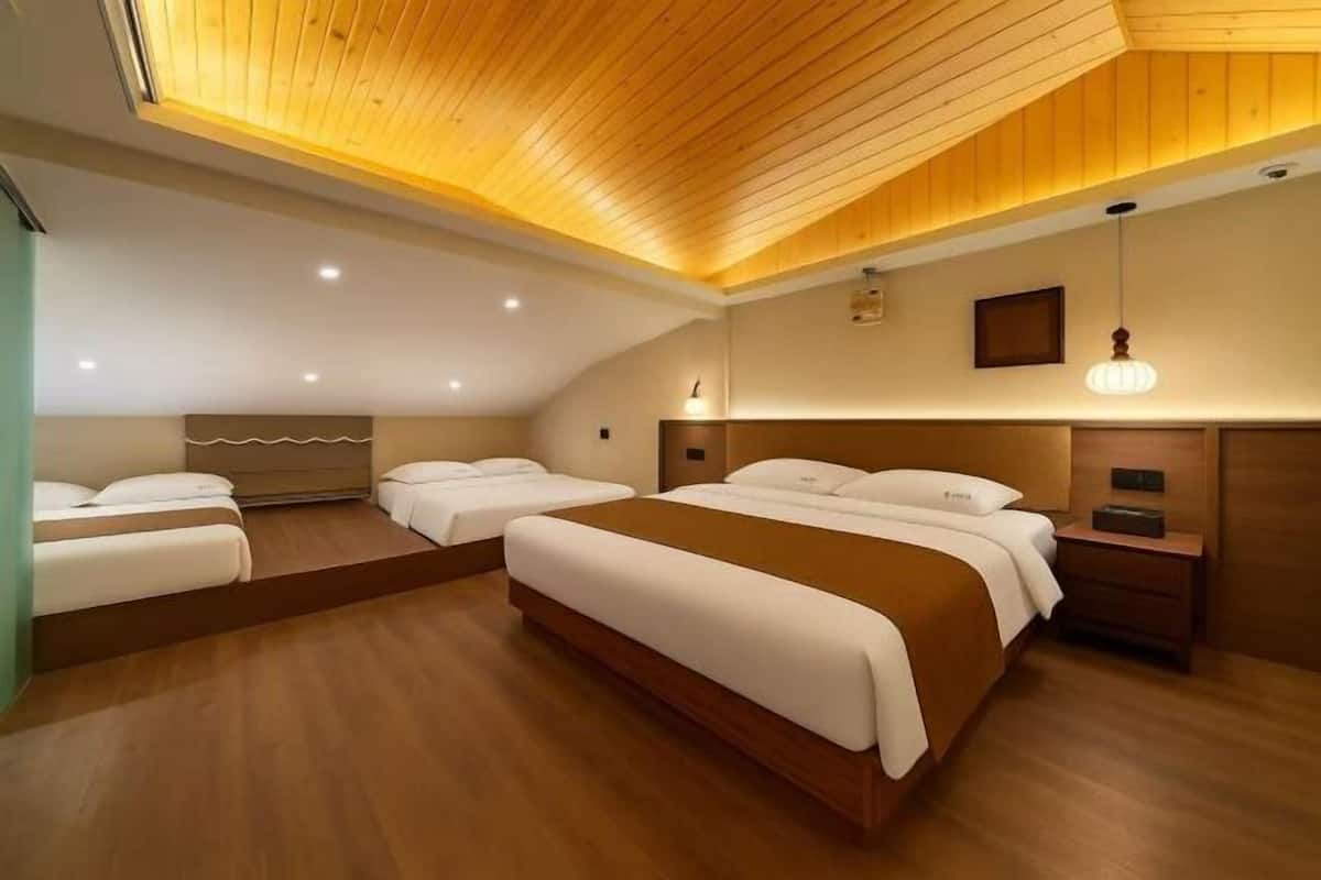 A hotel room with a wooden ceiling, two beds, a nightstand, and a wall-mounted light fixture.