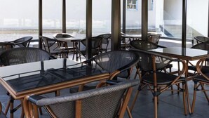 An indoor dining area with glass tables and wicker chairs, large windows, and a view of a building across a body of water. - Kulangsu Youran Bieyuan Vacation Apartment (Meihua Beach Neicuo'ao Pier) (Xiamen)
