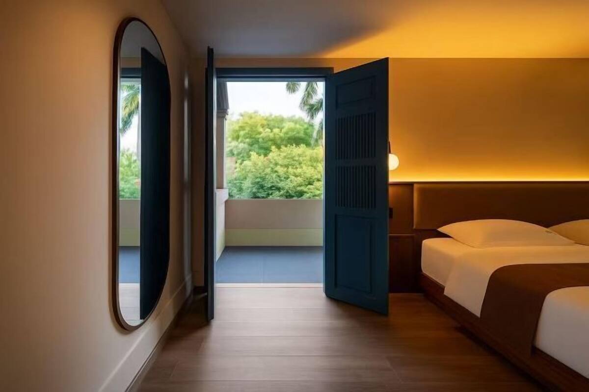A hotel room with a large bed, a view of greenery outside, and a door leading to a balcony.