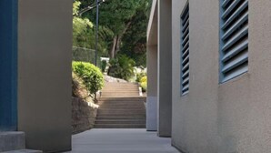 A corridor with steps leading to a staircase, flanked by walls with vents and a stone wall with greenery. - Kulangsu Youran Bieyuan Vacation Apartment (Meihua Beach Neicuo'ao Pier) (Xiamen)