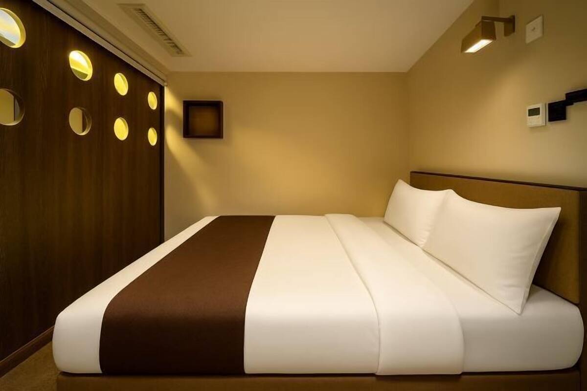 A hotel room with a large bed, a wooden panel wall with circular lights, a flat-screen TV, and a thermostat on the wall.