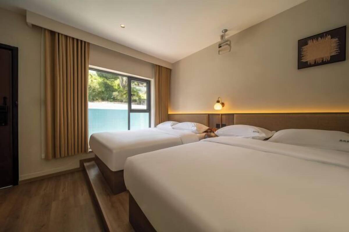 A hotel room with two beds, a window with curtains, a wall-mounted light, and a door.