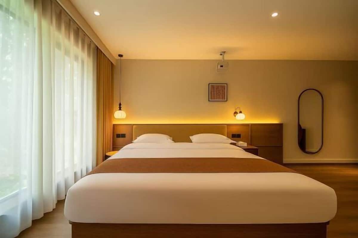 A hotel room with a large bed, bedside lamps, a mirror, and a window with curtains.