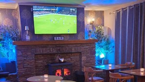 Un coin bar accueillant avec une cheminée en pierre, un téléviseur fixé au-dessus et des meubles en bois.