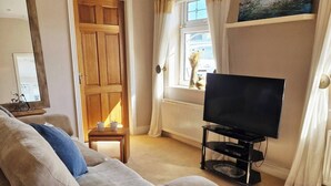 Un salon avec un canapé beige, un téléviseur posé sur un meuble, une petite table avec une tasse et un tableau accroché au mur.