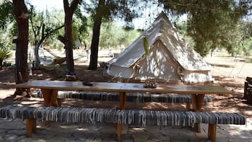A wooden picnic table with benches, a tent, and a hammock in a wooded area.