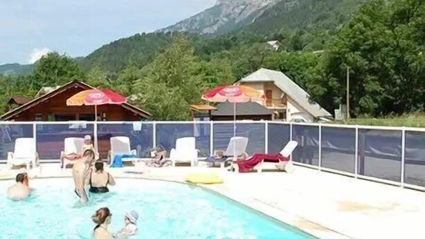Una piscina con gente, sillas de descanso y montañas al fondo.