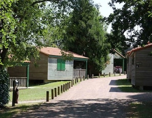 Una hilera de cabañas de madera con contraventanas verdes, un camino de grava que las conduce, y un cartel que indica un baño accesible para discapacitados.