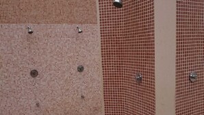 A shower area with tiled walls and floor, featuring multiple showerheads and a control panel.