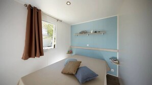 Ein Schlafzimmer mit einem Bett, einem Fenster mit Vorhängen, einem Regal mit Dekoration und einer Wandleuchte.