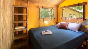 Ein Einzelbett mit blauer Bettdecke, Kissen und einem gefalteten Handtuch. Eine Holzregaleinheit befindet sich links vom Bett.