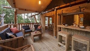 Eine Holzterrasse mit Sitzgelegenheiten im Freien, einer Bar und Blick auf die umliegenden Bäume.