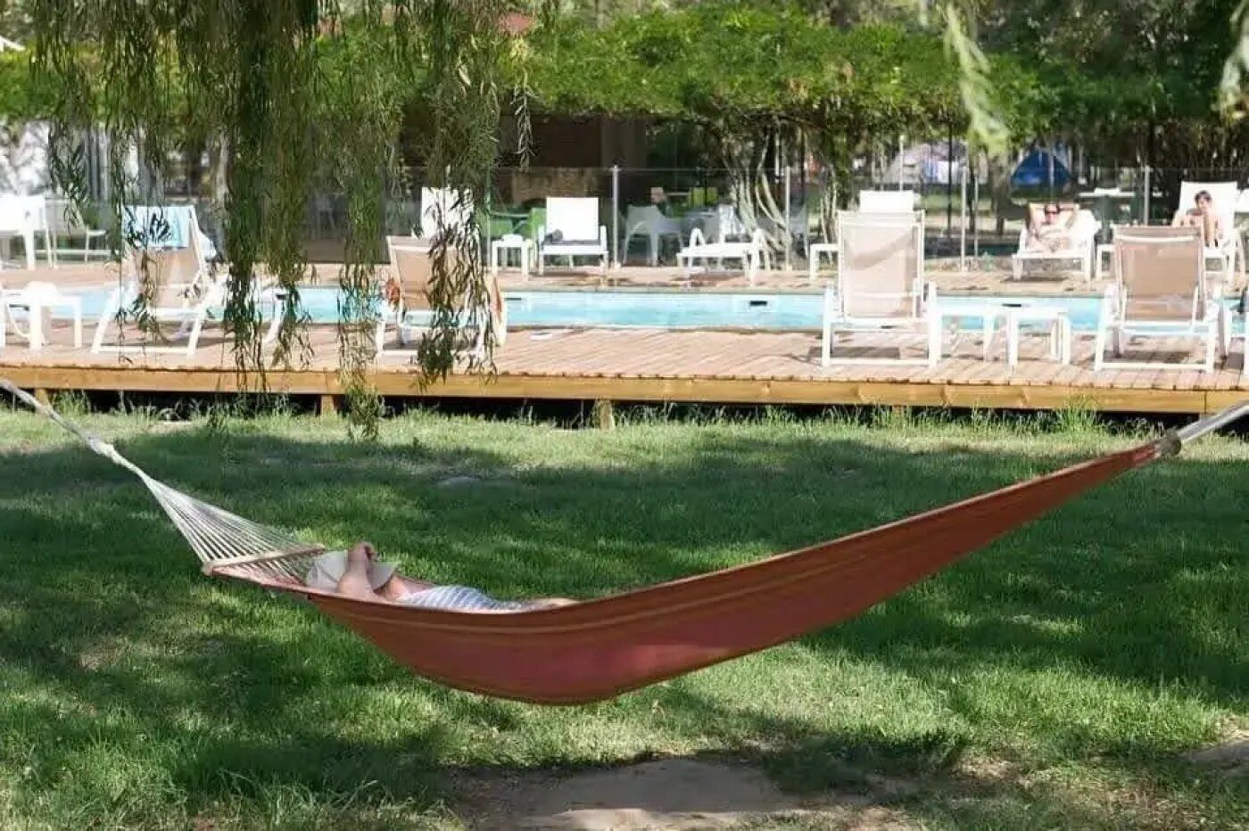 Un hamac posé sur l’herbe, avec une piscine et des chaises longues en arrière-plan.