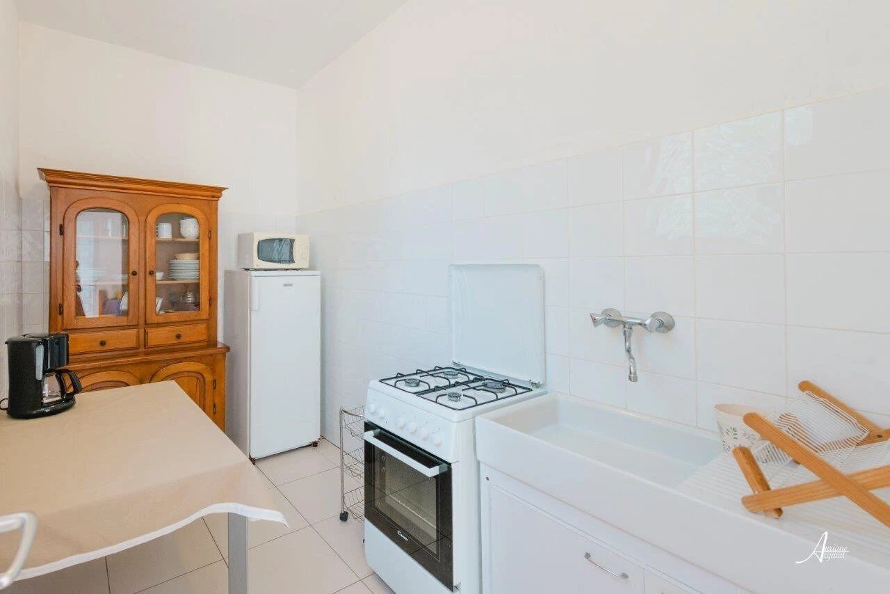 Une cuisine compacte équipée d’une cuisinière à gaz, d’un four à micro-ondes et d’un réfrigérateur. On y trouve un meuble en bois avec des portes en verre et une petite table avec une bouilloire.