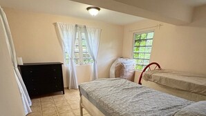 A small, well-lit room with two beds, a dresser, and a window with curtains.