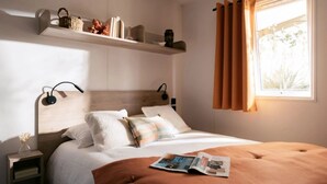 Ein ordentlich eingerichtetes Schlafzimmer mit einem hölzernen Kopfteil, einem Nachttisch mit Lampe, einem Fenster mit Vorhängen und einem Regal mit Dekoration.