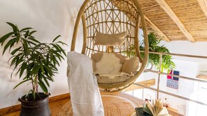 A room with a hanging chair, a potted plant, a woven rug, and a bookshelf with books and a small table. - 900 mt from the historic center of Tortolì and 5 km from all the most beautiful beaches. (Tortolì)