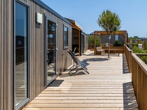 En moderne bygning med store glasdøre, en træterrasse og udendørs siddepladser.
