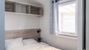 A bedroom with a bed, a bedside table, a wall-mounted shelf, and a window with blinds. - ZEcamping 3 étoiles piscine chauffée dog friendly locatif TV LV BBQ (Martigues)