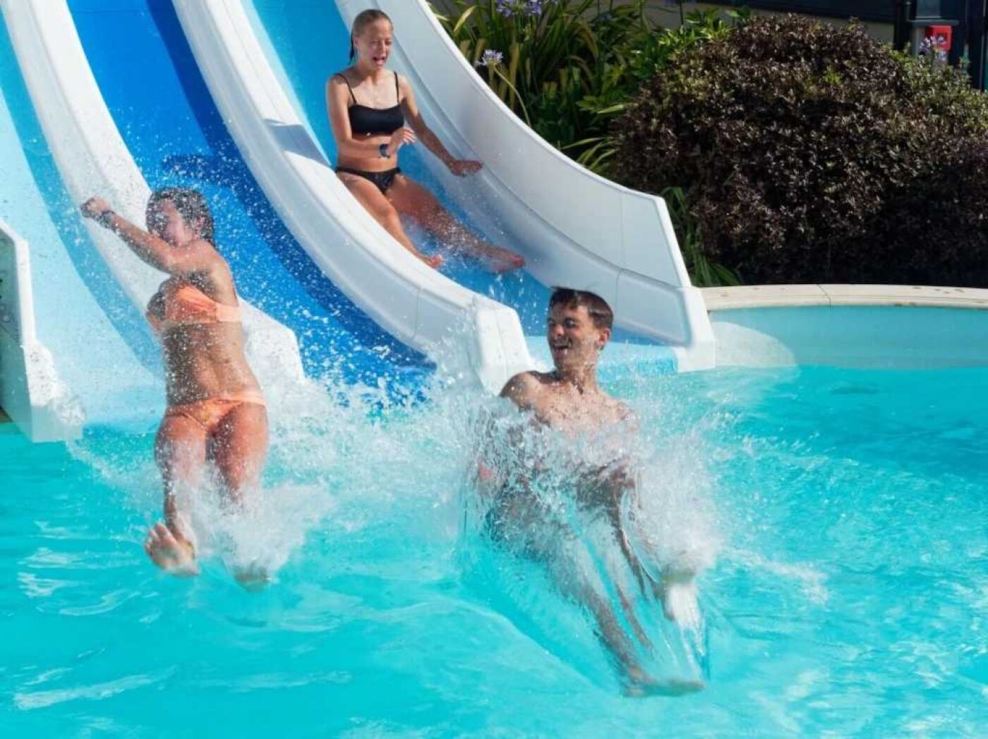 Eine Wasserrutsche an einem Pool mit klarem, blauem Wasser und einer weiß-blauen Rutsche.