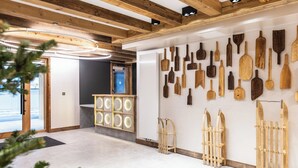 Een hal met houten balken in het plafond, een wand met diverse houten werktuigen, en een glazen deur naar buiten.