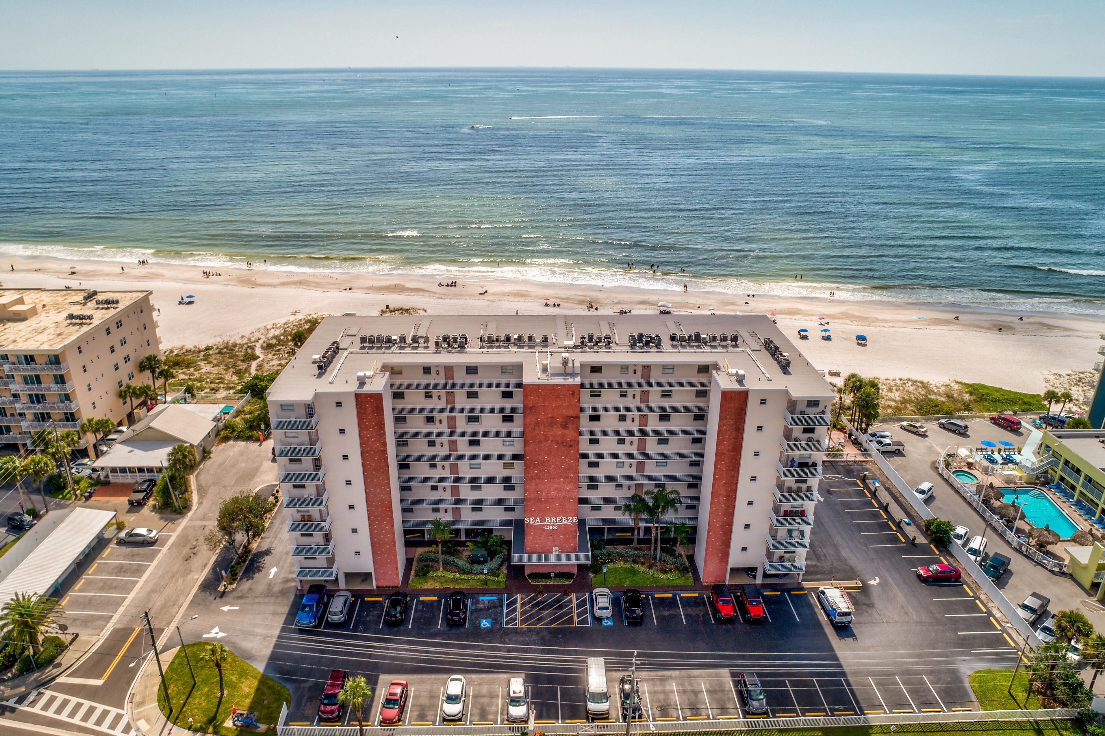 Ein Hotel mit einer zentralen roten und weißen Fassade, einem Parkplatz und Blick auf Strand und Meer.