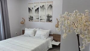 A bedroom with a bed, a nightstand, a lamp, a wall-mounted shelf, and a decorative plant. - 3BR Gulf Getaway | Elevator, Pool, Walk to IRB (Indian Rocks Beach)