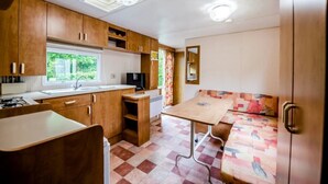 Cocina compacta de autocaravana con armarios de madera, un lavabo, una estufa y una zona de comedor con mesa y sofá.