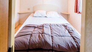 Una cama individual con cabecera, dos mesitas de noche y una lámpara de pared.