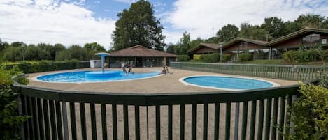 Zona de piscina amurallada con dos piscinas, rodeada por una terraza de madera y un edificio con tejado de azulejos al fondo.
