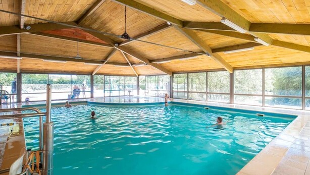 Una piscina interior con techo de madera y ventanas amplias.