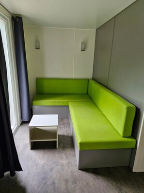 Une pièce moderne avec un canapé d’angle vert, une table basse blanche et une grande fenêtre avec des rideaux.