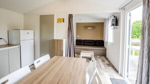 Une cuisine compacte comprenant un réfrigérateur, une table à manger avec des chaises, un petit meuble blanc et un canapé à l’arrière-plan.