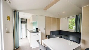 A compact kitchen with a microwave, a small stove, and a sink. There is a dining area with a table and chairs, and a seating area with a bench.