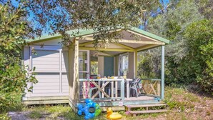 Une petite cabane à un seul étage, dotée d’un porche, d’une table et de chaises, et entourée d’arbres et d’arbustes.