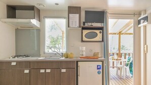 Una cocina compacta con microondas integrado, un refrigerador pequeño y una ventana con persianas.