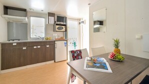 Cocina compacta con microondas, estufa y refrigerador. Hay una mesa de comedor con una revista y fruta.