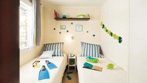 A child's bedroom with two beds, star decorations, a shelf with books, and a window. - ZEcamping 3 étoiles familial toboggans locatif TV clim 26m2 4 pers (Sussargues)