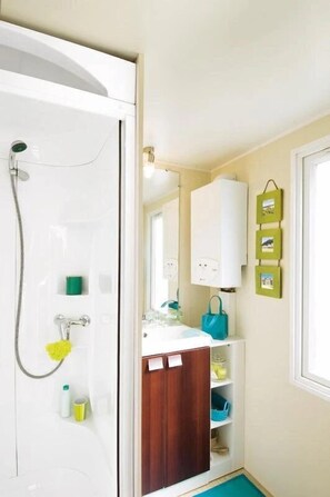 Une salle de bain équipée d’une douche, d’un lavabo, d’un miroir et d’un meuble de rangement.