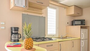 A compact kitchen with a yellow countertop, a gas stove, a microwave, and a refrigerator. - ZEcamping 3 étoiles toboggans club enfant locatif TV clim 26m2 4 pers (Sussargues)