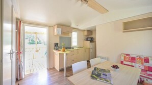 A compact kitchen with a dining area, a small refrigerator, and a microwave. - ZEcamping 3 étoiles toboggans club enfant locatif TV clim 26m2 4 pers (Sussargues)