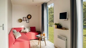 Una sala de estar moderna con un sofá rosa, una mesita redonda con una bebida y un televisor montado en la pared.