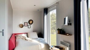 Un dormitorio con cama, mesita de noche, ventana y televisor instalado en la pared.
